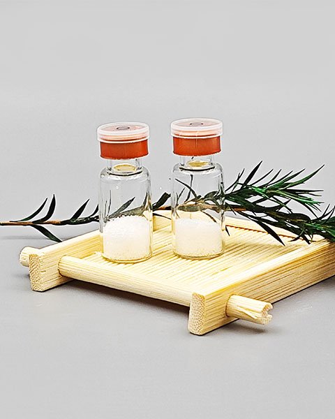 Two vials of lyophilized peptide powder displayed on a bamboo tray with herbal decoration