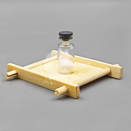 Freeze-dried melatonin powder sample in a glass vial on bamboo tray with gray background